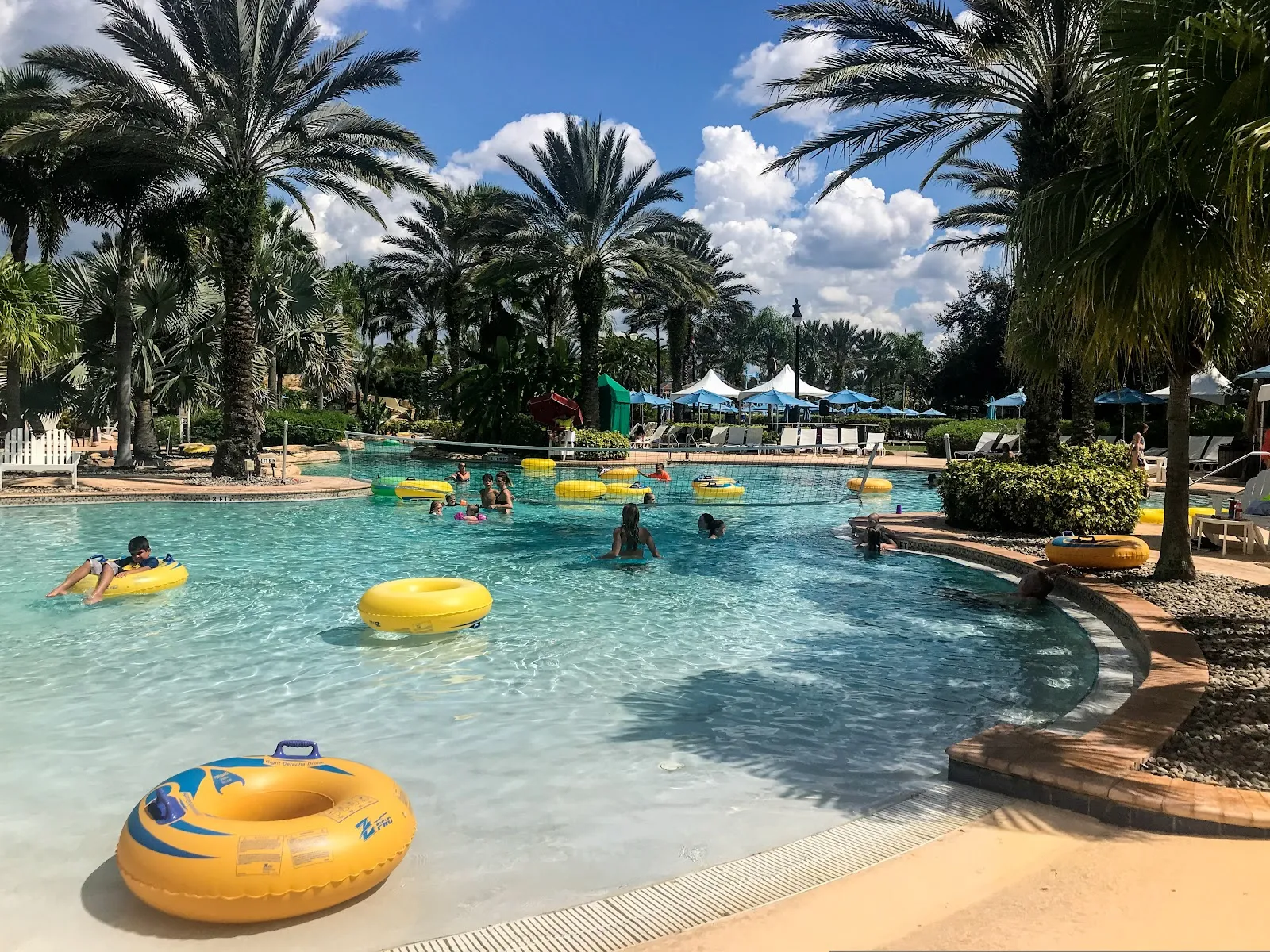 Parque aquático na Tailândia: diversão para toda a família Parque aquático de resort na Tailândia com palmeiras, crianças e adultos a divertir-se na água